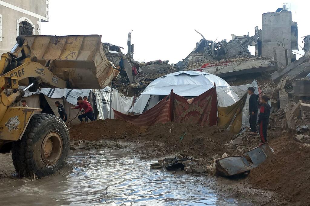 Los niños se refugian cerca de una tienda improvisada entre los escombros y las inundaciones, mientras las fuertes lluvias azotan Gaza.